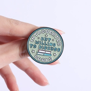 Green enamel pin with Introverted But Willing To Discuss Books slogan held in hand