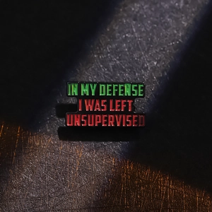 Gros plan d'un pin's en émail avec texte humoristique IN MY DEFENSE I WAS LEFT UNSUPERVISED
