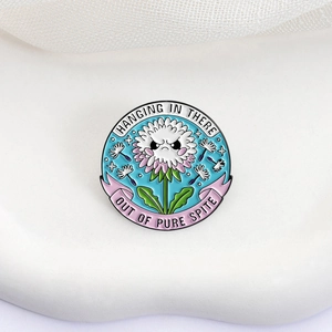 Angry dandelion enamel pin with Hanging in there text on minimalist fabric background