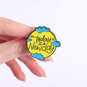 Close-up of a yellow enamel pin with Today Is A New Day quote and blue clouds