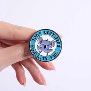 Close-up of a blue round enamel koala badge with 100% Certified Koala-ty-Pun text