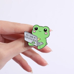 Macro detail of cartoon frog enamel pin with Just Doing My Silly Little Tasks text