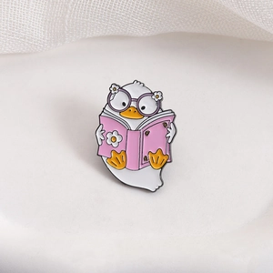 Cute white duck enamel pin wearing purple glasses and reading a pink flower book