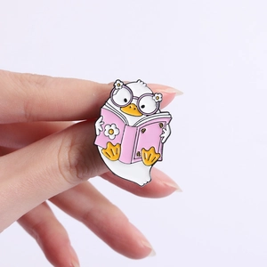 Cute cartoon duck enamel pin wearing glasses reading a pink book with flower detail