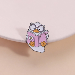 Cute pink enamel duck brooch with glasses reading a book on a warm background