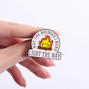 Dettaglio della spilla smaltata con Calcifer e testo 'May the bridges I burn light the way'