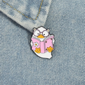 Cute pink enamel duck brooch reading a book pinned on blue denim jacket fabric