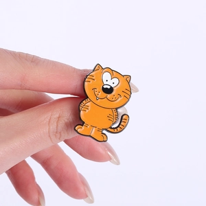 Nahaufnahme einer kleinen orangen Emaille-Katzenbrosche mit Herzaugen in der Hand