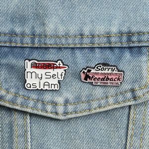 Detail von zwei lustigen Emaille-Pins mit Slogan an einer blauen Jeansjacke