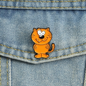 Nahaufnahme einer orangefarbenen Katzen-Emaille-Anstecknadel an einer Jeansjacke