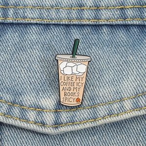 Detail of iced coffee enamel pin with 'Icy Coffee and Spicy Books' text on denim fabric