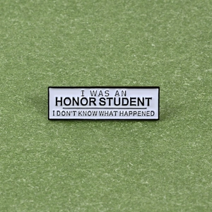 Macro shot of rectangular enamel pin with humorous I Was An Honor Student text on green background