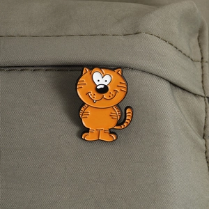 Detaillierte Nahaufnahme einer süßen orangefarbenen Emaille-Katzenbrosche auf grünem Stoff