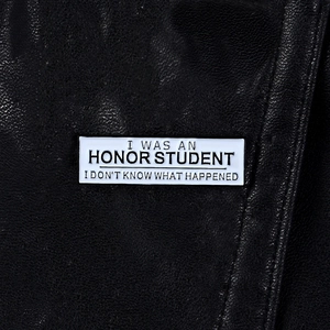 Close-up of a rectangle enamel pin with funny quote on black textured leather