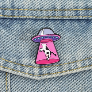 Détail du pin's émaillé OVNI enlevant une vache sur une veste en jean bleue