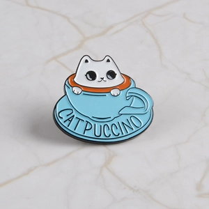 Catpuccino enamel pin featuring a cute white cat in a blue coffee cup on marble