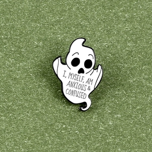 Ghost enamel pin with text 'I, MYSELF, AM ANXIOUS & CONFUSED' on green grass background