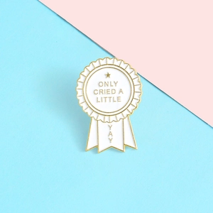 Détail d'une broche en émail en forme de médaille avec texte Only Cried A Little sur fond