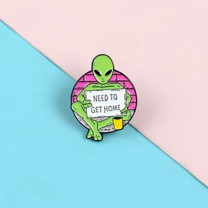 Cartoon green alien enamel pin holding a Need To Get Home sign with a yellow coffee cup