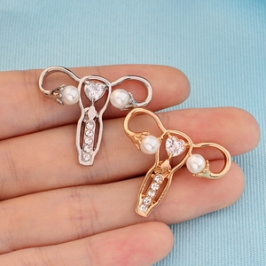 Golden and silver uterus brooches with heart crystal and pearls held in hand