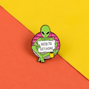 Detail of green alien enamel pin with NEED TO GET HOME sign on pop art background