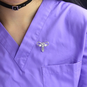 Creative silver uterus brooch with pearls and crystals pinned on a purple medical uniform