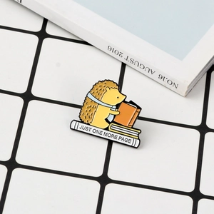 Détail du pin's hérisson en émail avec texte posé sur un livre dans un décor
