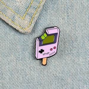 Purple Game Boy popsicle enamel pin on blue denim fabric background in high detail