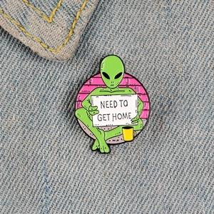 Round enamel alien pin badge with Need To Get Home sign on blue denim background