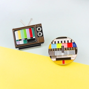 Emaille-Pin-Set im Retro-TV-Design mit farbigen Testbildmustern auf blau-gelbem Hintergrund