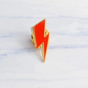 Minimalist red lightning bolt enamel brooch with gold finish on marble surface