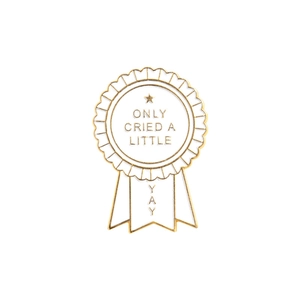 Close-up of a white enamel medal brooch featuring Only Cried A Little and YAY text engraving