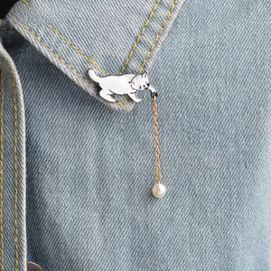 Vue détaillée d'une broche chat en émail blanc avec chaîne dorée et perle sur denim