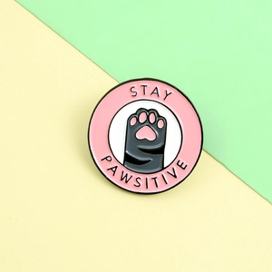Close-up of the Stay Pawsitive pink enamel pin with a black cat paw print design