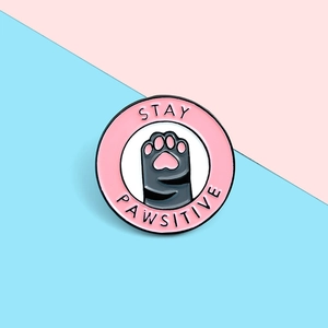 Close-up of a pink Stay Pawsitive enamel pin featuring a cute cat paw design