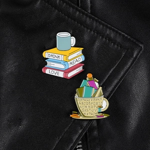 Vue rapprochée de broches émaillées livre et tasse de café sur fond de texture cuir noir