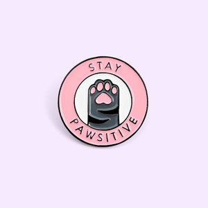 Épingle ronde en émail avec motif de patte de chat et texte Stay Pawsitive sur fond violet