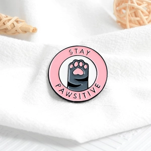 Round pink enamel pin with black cat paw and Stay Pawsitive text for backpacks