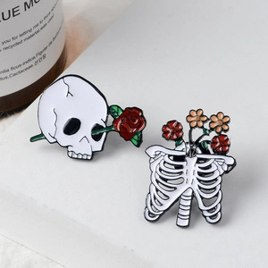 Gothic skull with red rose and ribcage floral enamel pins set against a white background