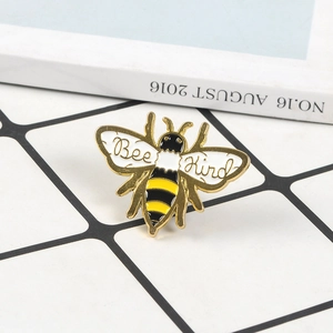 Broche abeille dorée en émail avec texte Bee Kind sur fond de grille blanche épurée
