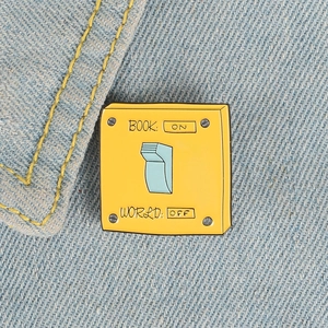 Detail of yellow switch enamel pin on denim showing 'BOOK: ON WORLD: OFF' text