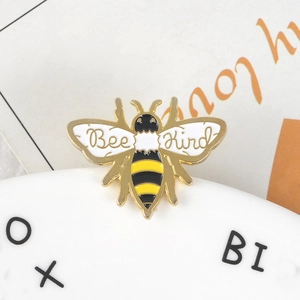 Détail macro d'une broche abeille en émail avec placage or et texte Bee Kind sur les ailes