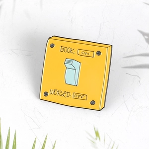 Retro yellow enamel pin featuring creative wall light switch design with BOOK ON text