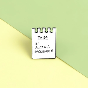 Detail of creative notepad enamel pin with hand-written motivational text on colorful background
