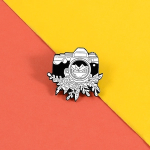 Detail of camera enamel pin featuring rose flowers and a mountain landscape scenery