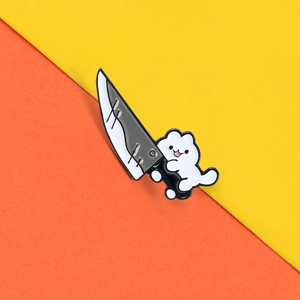 Detail of creative cartoon white cat enamel pin holding a small knife with smooth finish