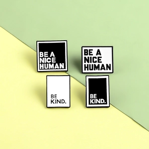 Close-up of metal enamel pins with Be A Nice Human and Be Kind text designs