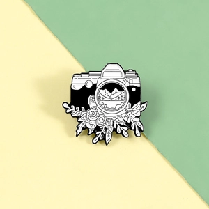 Detailed close-up of a camera enamel pin featuring mountain landscape and floral accents