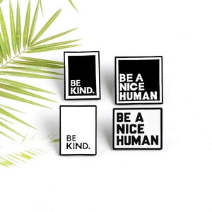 Macro view of black and white Be Kind enamel pins with green palm leaf decor