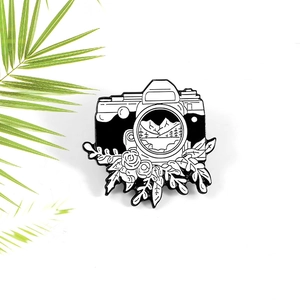 Enamel camera brooch featuring mountain forest scenery and roses on a white background